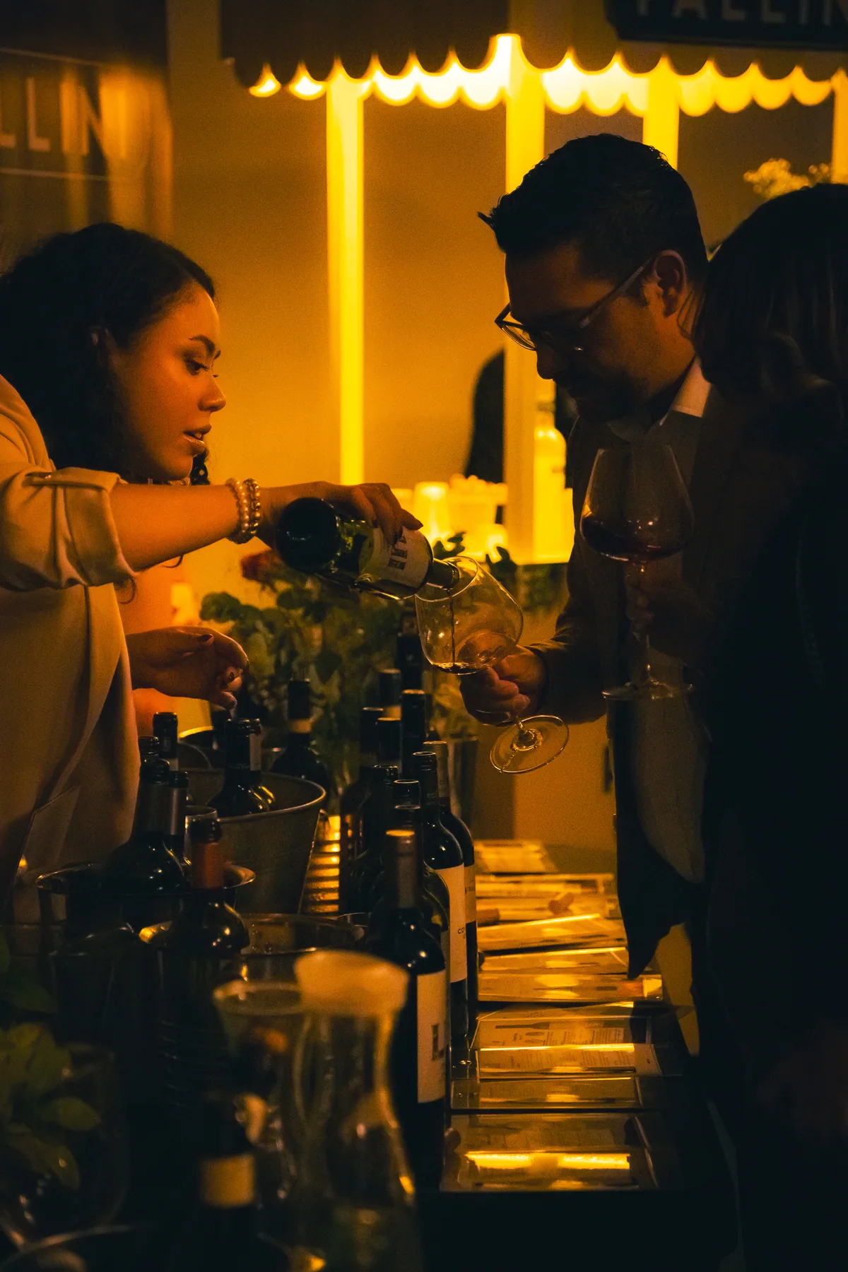 Dos asistentes conversan junto a una mesa de vinos durante un evento nocturno.