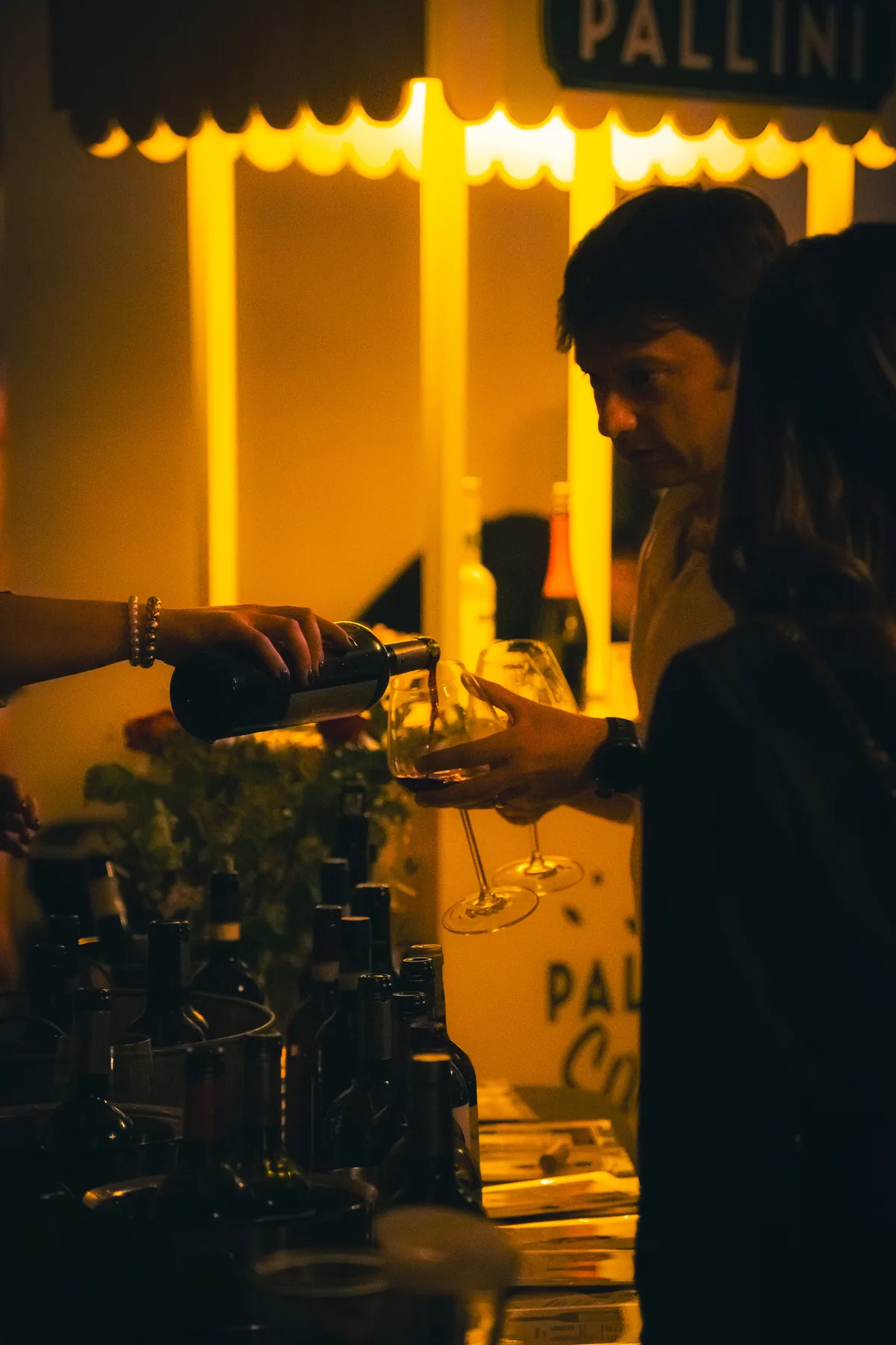 Servicio de vino junto a una pared de botellas y luz cálida.