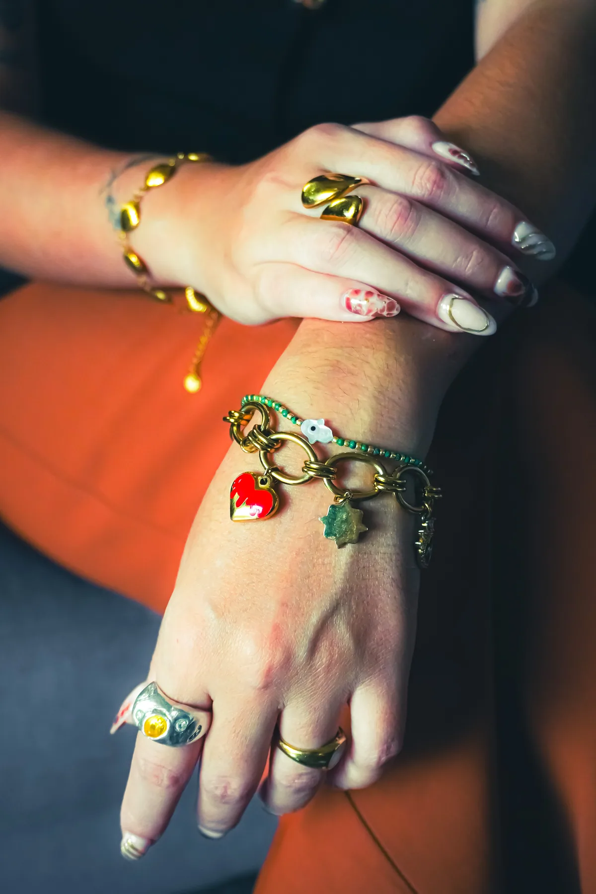 Manos con anillos y pulseras coloridas sobre una prenda roja.