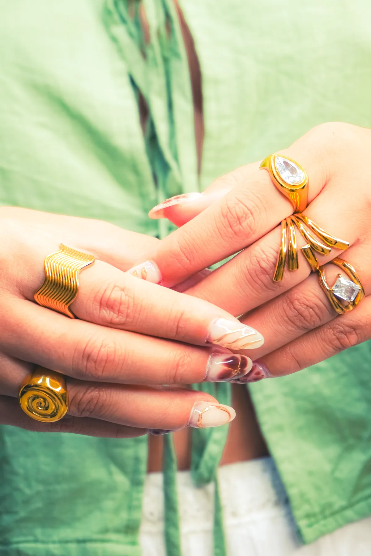 Detalle de un anillo dorado lucido en una mano junto a una prenda verde.
