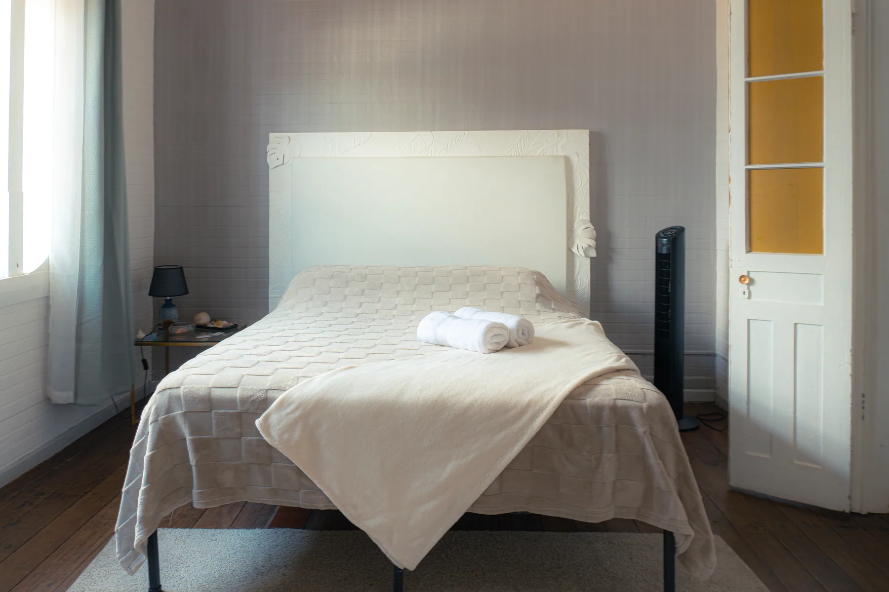 Cama blanca junto a una ventana en una habitación de alojamiento.