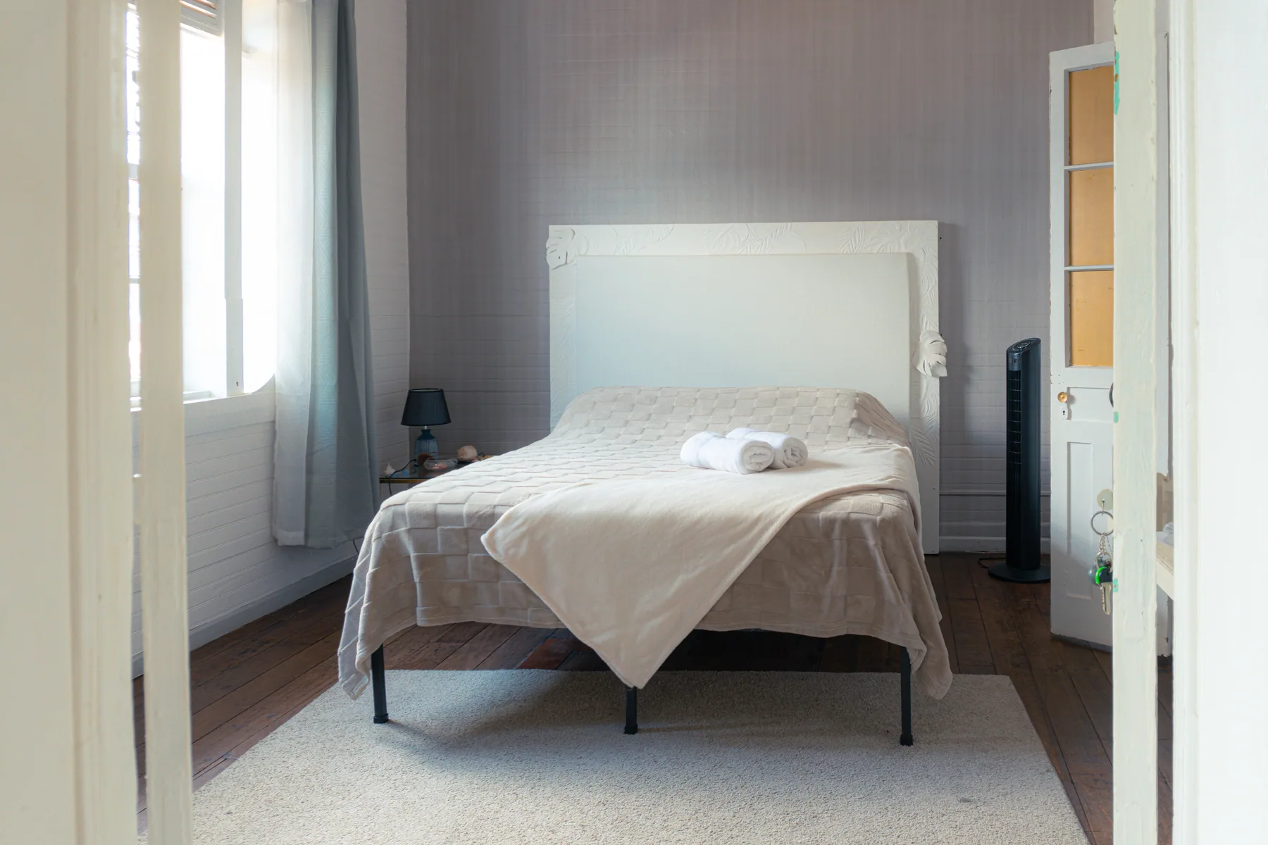 Cama blanca fotografiada desde la entrada de una habitación.