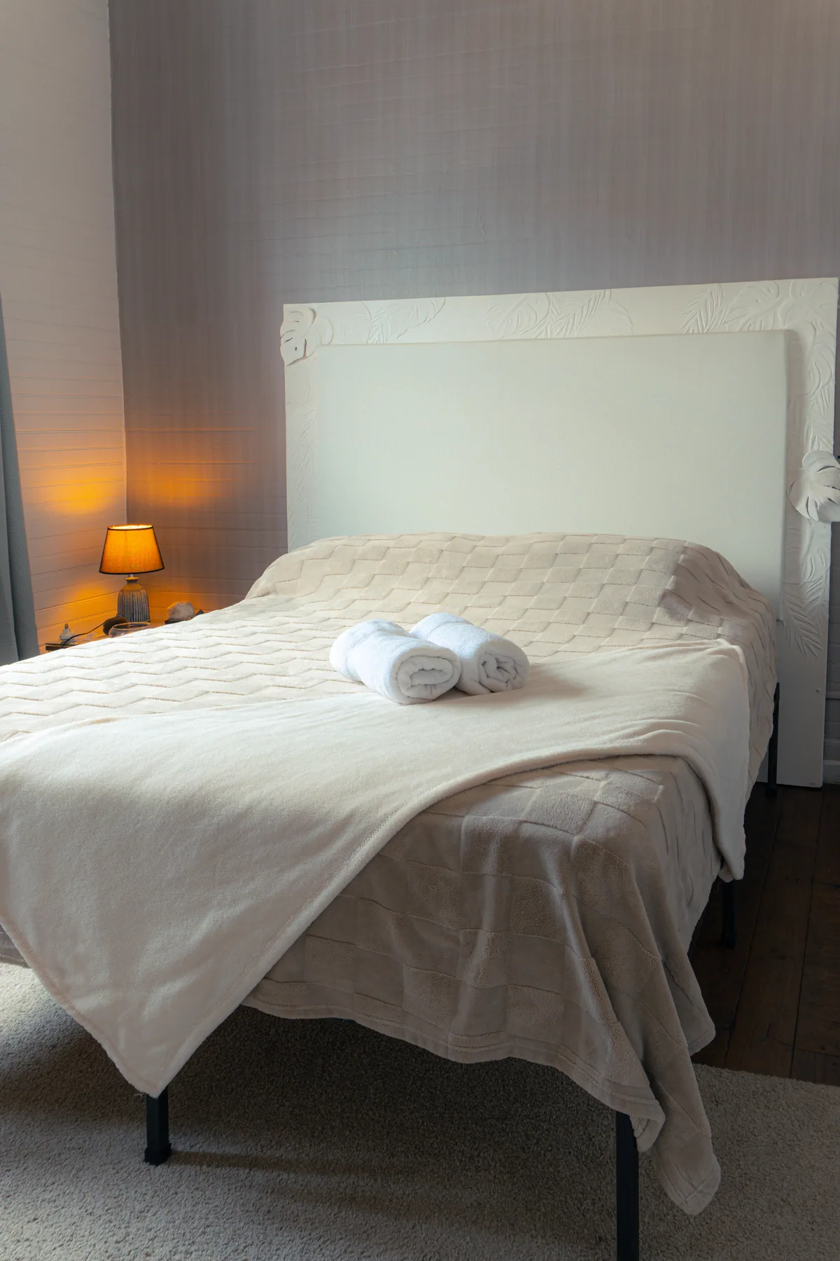 Habitación con cama blanca y luz cálida junto a la pared.