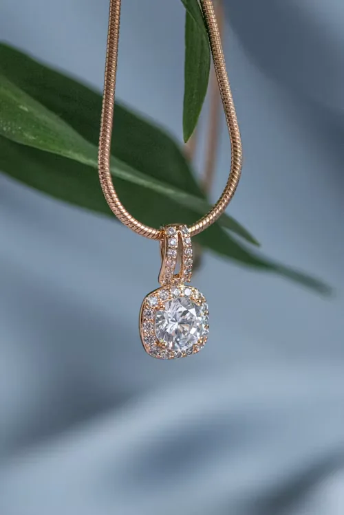 Cadena rosa con dije de piedra clara entre hojas verdes