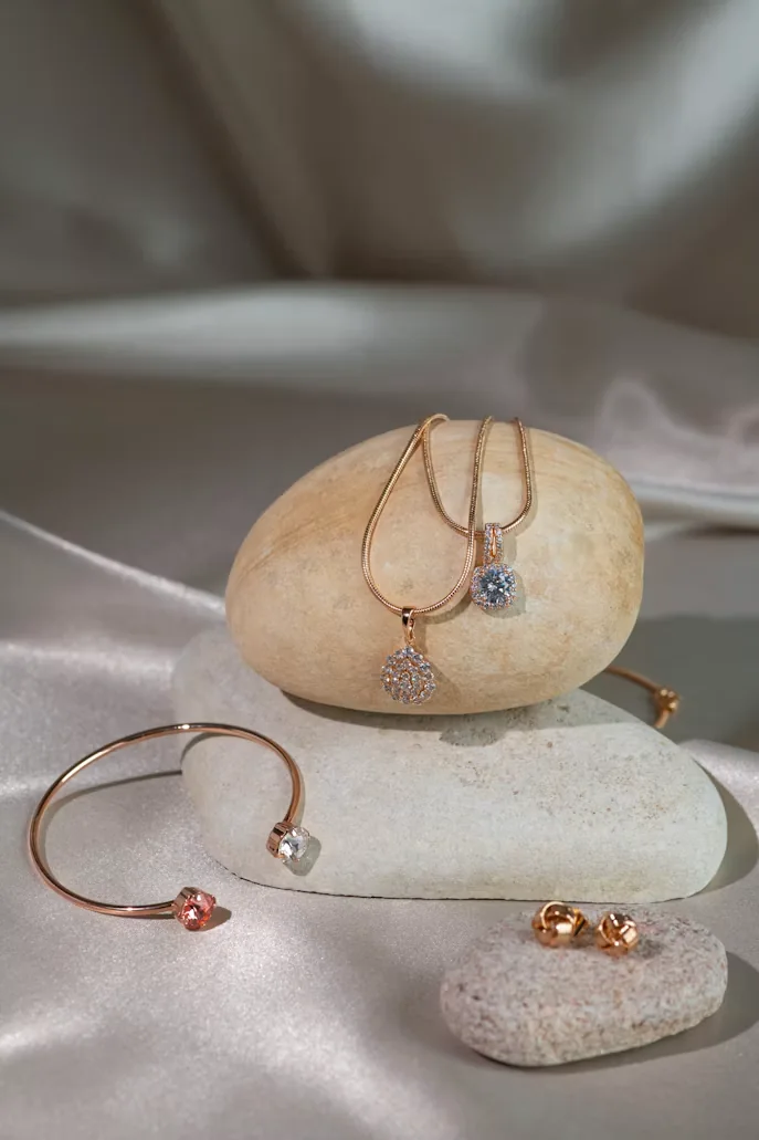 Conjunto de joyería en tono oro rosa con dijes y pulsera sobre piedras