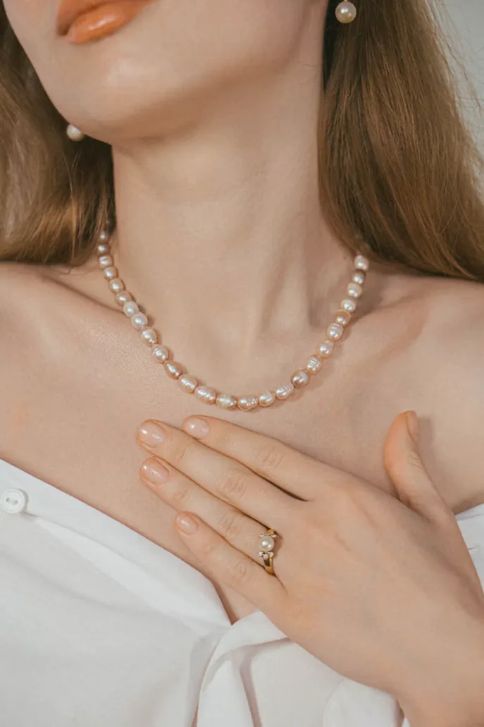 Collar de perlas y anillo lucidos con una blusa blanca